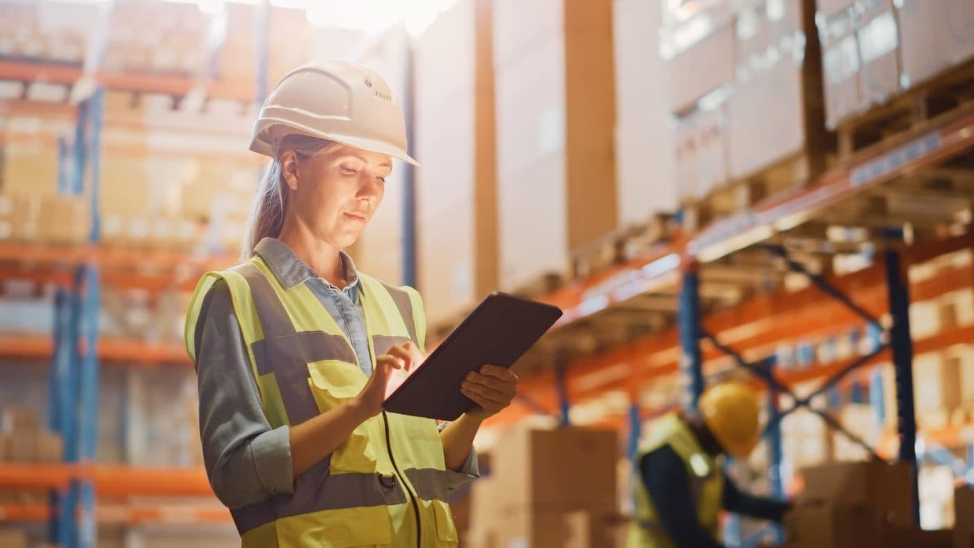 Warehouse operative checking stock against a tablet in a racking aisle