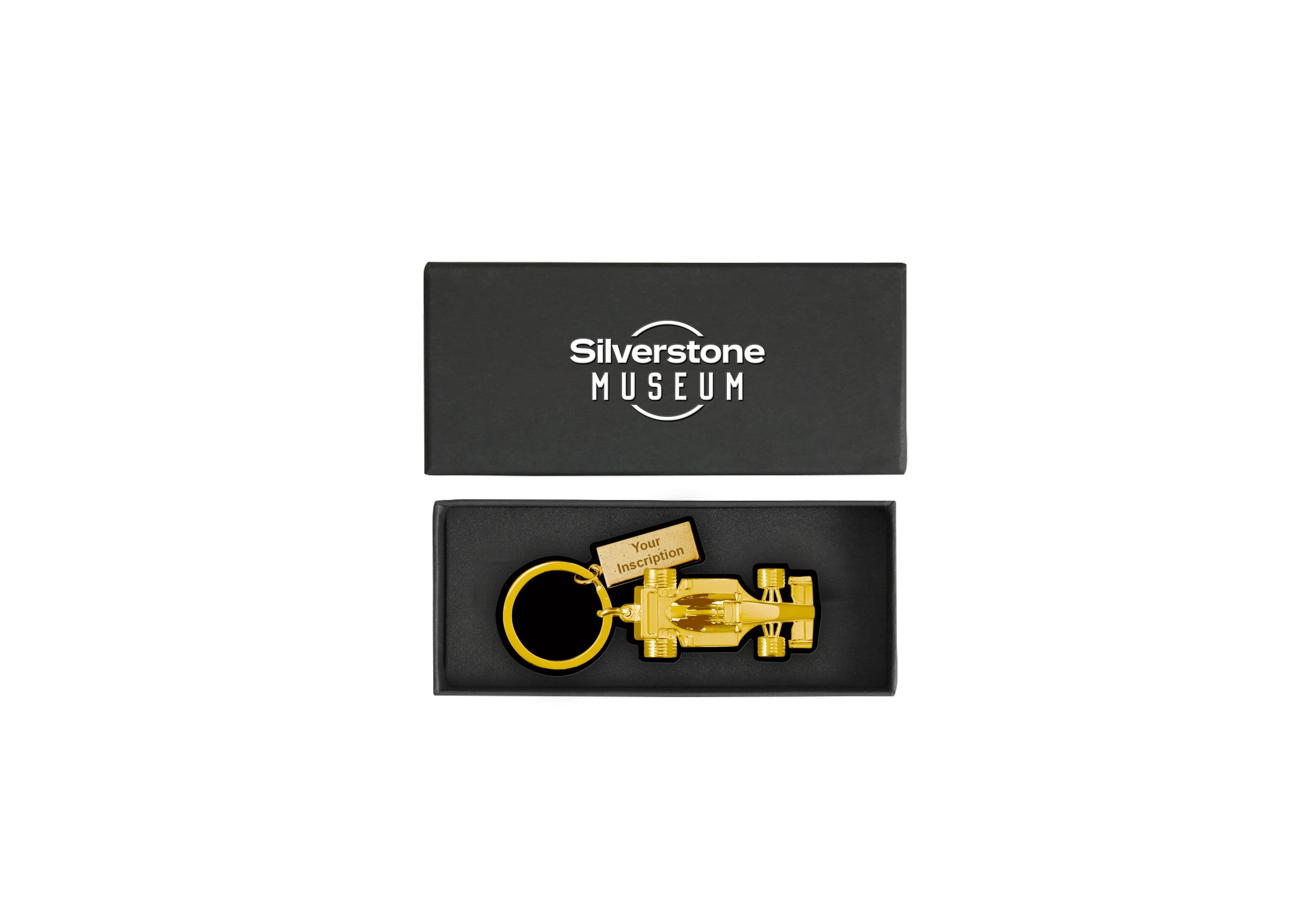 Gold-tone racing car keyring with a personalised inscription tag, displayed inside a black presentation box with a Silverstone Museum-branded lid.