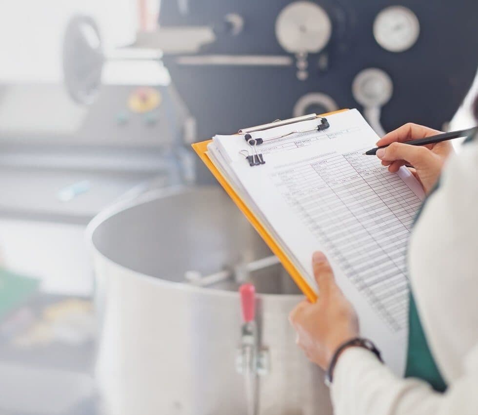Quality control engineer recording findings on a clipboard beside product on a production line